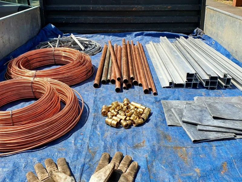 Arranged non-ferrous scrap metals including copper wire, brass fittings and aluminium extrusions laid out in natural sunlight